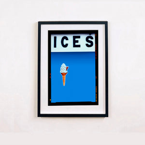 Black framed photograph by Richard Heeps.  At the top black letters spell out ICES and below is depicted a 99 icecream cone sitting left of centre against a sky blue coloured background.  
