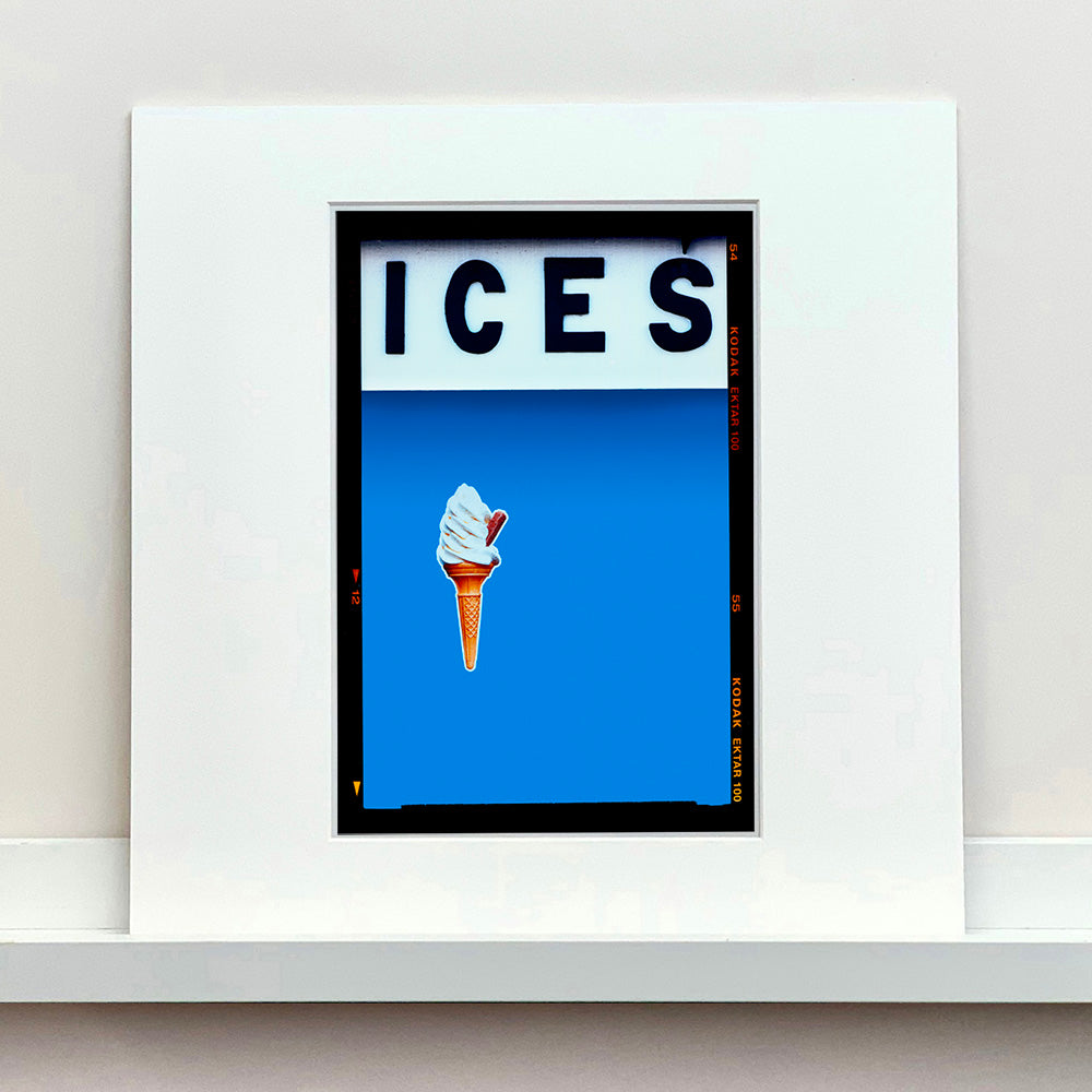 Photograph by Richard Heeps.  At the top black letters spell out ICES and below is depicted a 99 icecream cone sitting left of centre against a sky blue coloured background.  
