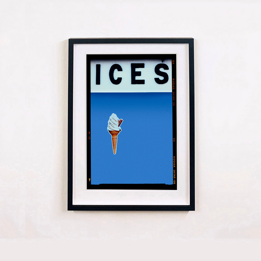 Black framed photograph by Richard Heeps.  At the top black letters spell out ICES and below is depicted a 99 icecream cone sitting left of centre against a baby blue coloured background.  