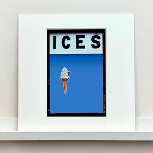 Mounted photograph by Richard Heeps.  At the top black letters spell out ICES and below is depicted a 99 icecream cone sitting left of centre against a Baby Blue coloured background.  