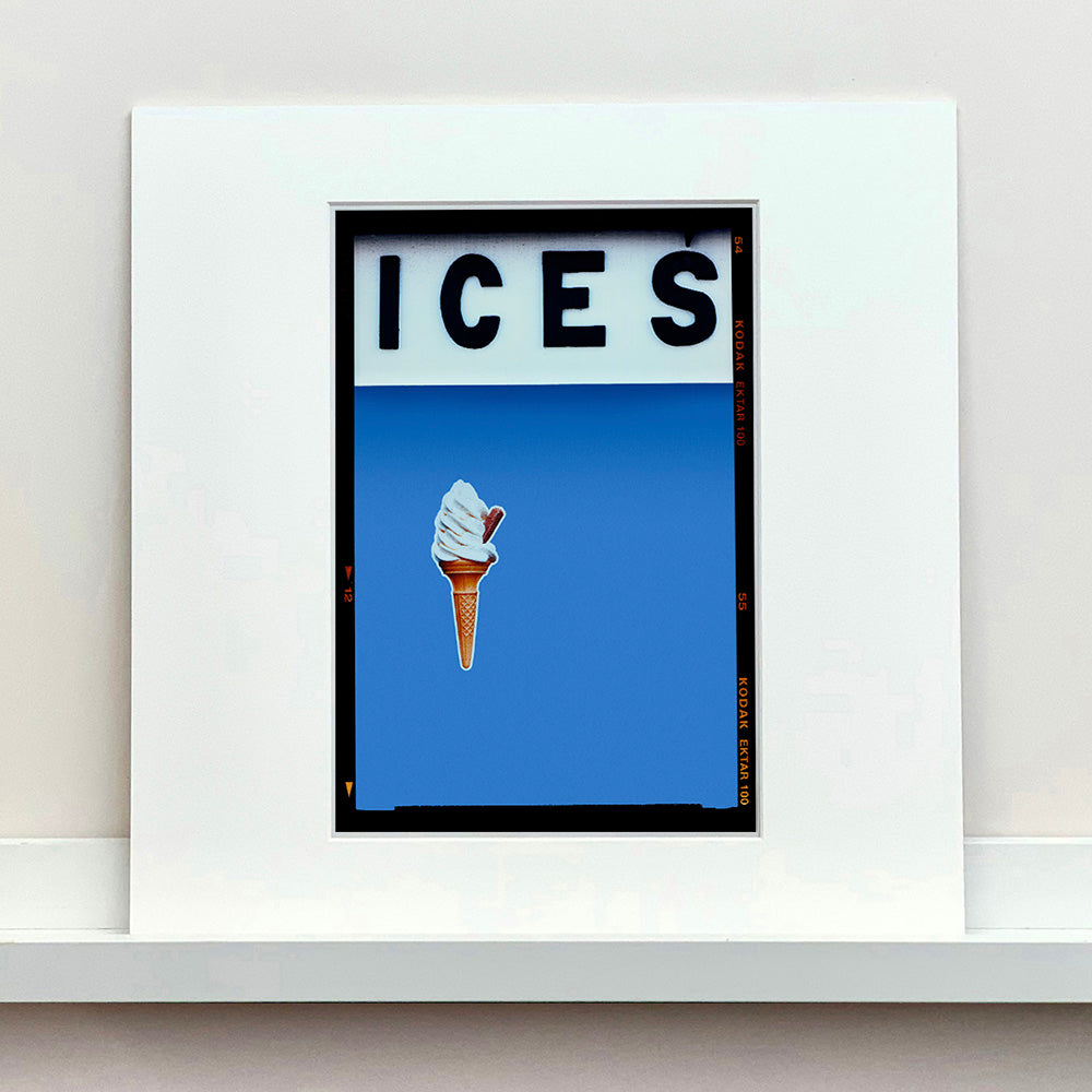 Mounted photograph by Richard Heeps.  At the top black letters spell out ICES and below is depicted a 99 icecream cone sitting left of centre against a Baby Blue coloured background.  