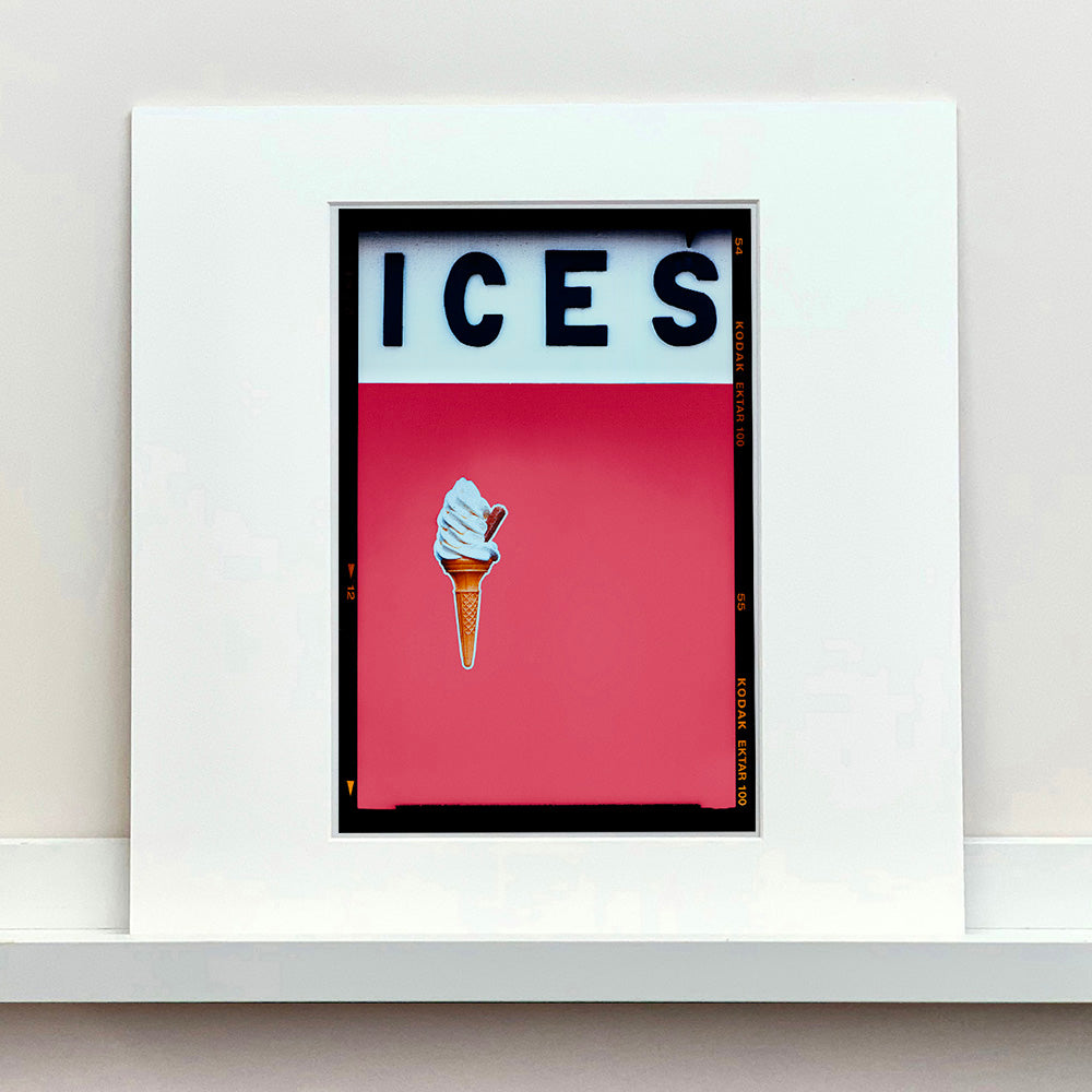 Mounted photograph by Richard Heeps.  At the top black letters spell out ICES and below is depicted a 99 icecream cone sitting left of centre against a coral coloured background.  