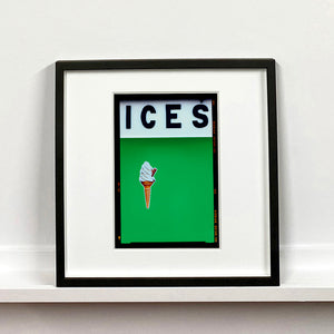 Black framed photograph by Richard Heeps.  At the top black letters spell out ICES and below is depicted a 99 icecream cone sitting left of centre against a green coloured background.  