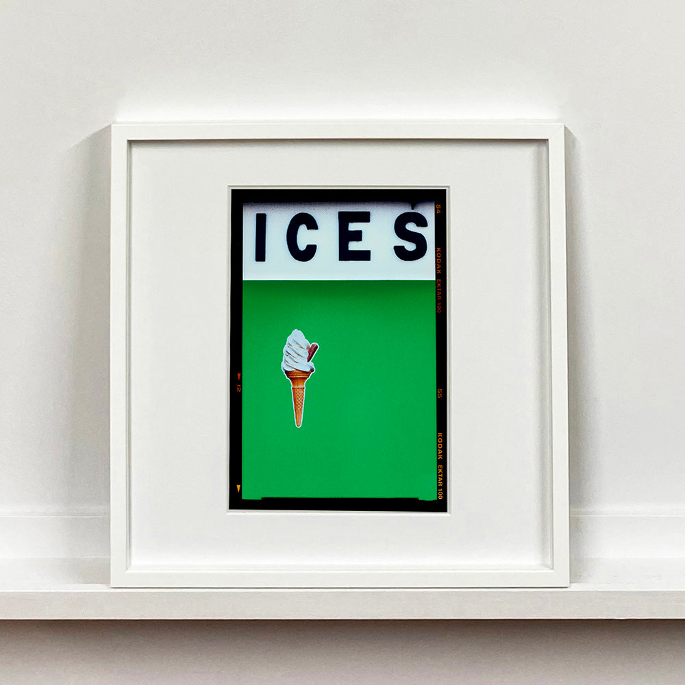 White framed photograph by Richard Heeps.  At the top black letters spell out ICES and below is depicted a 99 icecream cone sitting left of centre against a green coloured background.  