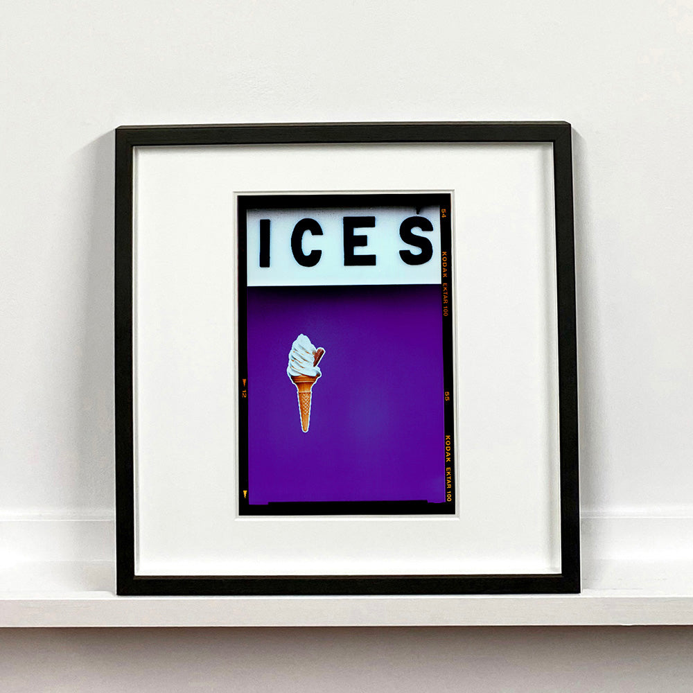 Black framed photograph by Richard Heeps.  At the top black letters spell out ICES and below is depicted a 99 icecream cone sitting left of centre against a purple coloured background.  