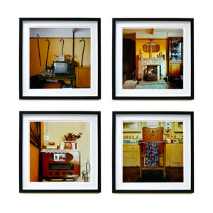 Four black framed photographs by Richard Heeps. From Richard's series Ordinary Places, the four photos capture vintage indoor scenes. The first one is a television, with 4 walking sticks and a bed pan hanging from the picture rail behind, the second one is a sitting room with a fireplace and candlesticks, the third is a vintage radio with a telephone on top of it, the fourth photo is of a brown leather barbers chair with the colourful cutting gown hanging over a bar on the chair.