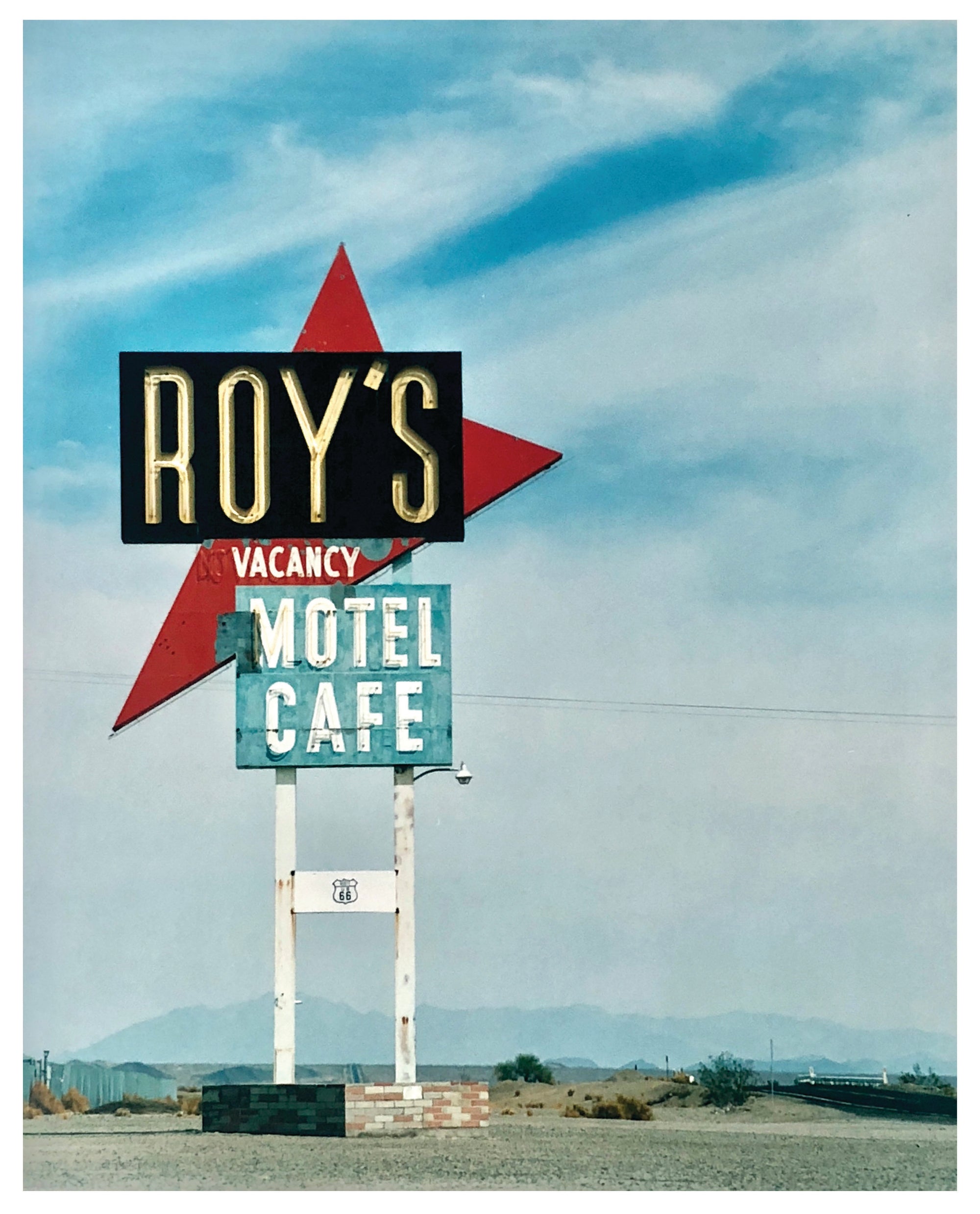 Photograph by Richard Heeps. A roadside sign on Route 66 in America. The word ROY'S appears in a black sign with a big red arrow pointing to the left ground, below this VACANCY and on a green square the words MOTEL and CAFE.