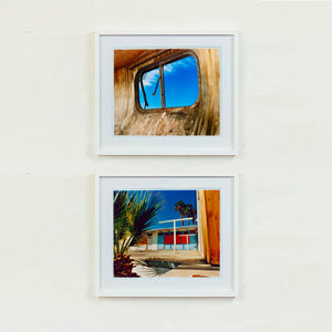 Two white framed photographs by Richard Heeps. The top photograph is of an interior of an eroded trailer, looking through the broken window to a deep blue sky. The bottom photograph is the outside of a brightly coloured motel, set against a blue sky. There is a palm tree at the side front of the scene.