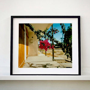 Black framed photograph by Richard Heeps. A flowering bougainvillea hangs outside a motel entrance.