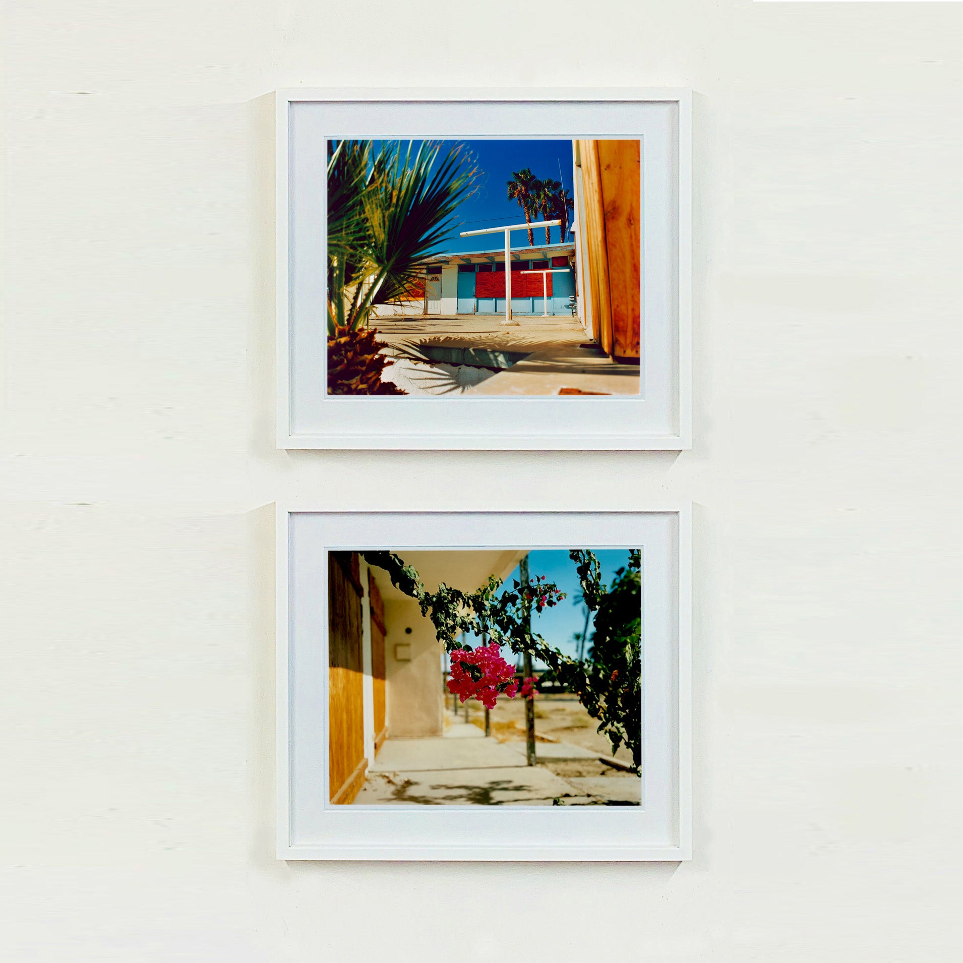 Two white framed photographs by Richard Heeps. The top photograph is of a colourful but derelict vintage motel sitting in the blue Californian sun. Palm trees appear behind and to the side. The bottom photograph has the motel room doors on the left hand side over top is the porch and in the centre of the photo hangs a beautiful pink bougainvillea.