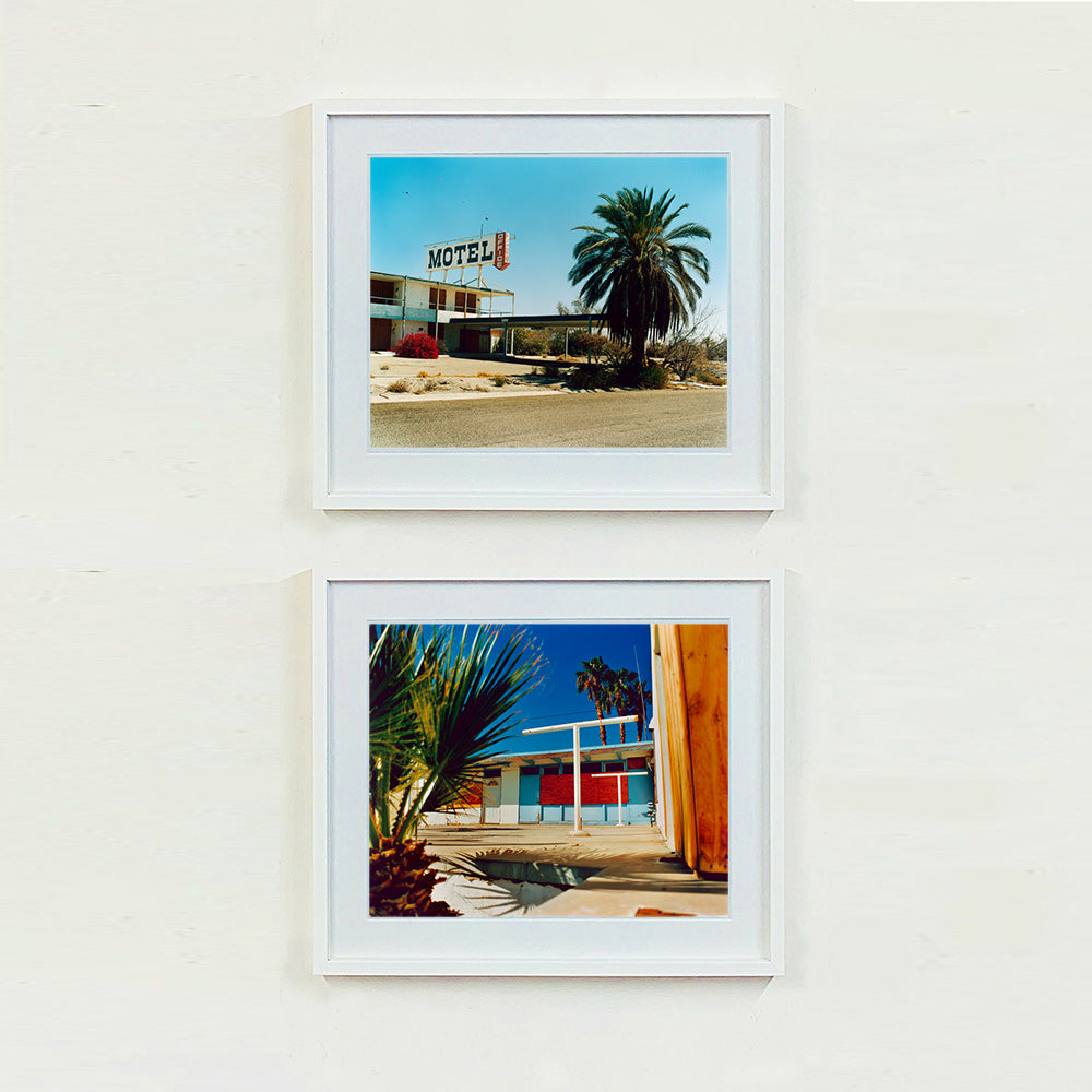 Two white framed photographs by Richard Heeps. The top photograph is of a derelict motel office sitting on a dusty American road. A large palm tree sits at the front of the office's walkway. The bottom photograph is the outside of a derelict motel, the building has strong colours on it and sits against a beautiful blue sky. There is a palm tree behind the motel and sitting to the left of the scene.