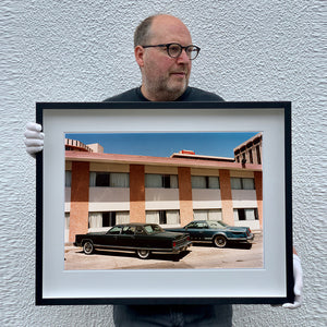 Black framed photograph by Richard Heeps. This retro photograph has two classic Lincoln cars parked outside a hotel in Las Vegas. The photograph is being held by the photographer.