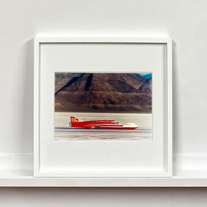 White framed photograph by Richard Heeps.  A Red Ferguson Racing Streamliner sits on a smooth salt flat with mountains in the background.