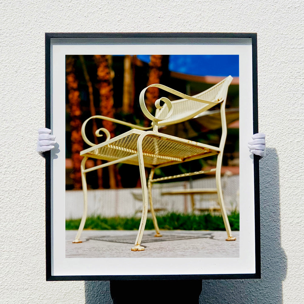 Photograph by Richard Heeps. A cream chair sits on hard standing, behind the chair and slightly out of focus is lush green grass and warm red tree trunks.