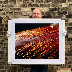 Photograph held by photographer Richard Heeps. The photograph is of a brown metal surface with water droplets on. The lighting makes the droplets appear in different colours of orange and brown.