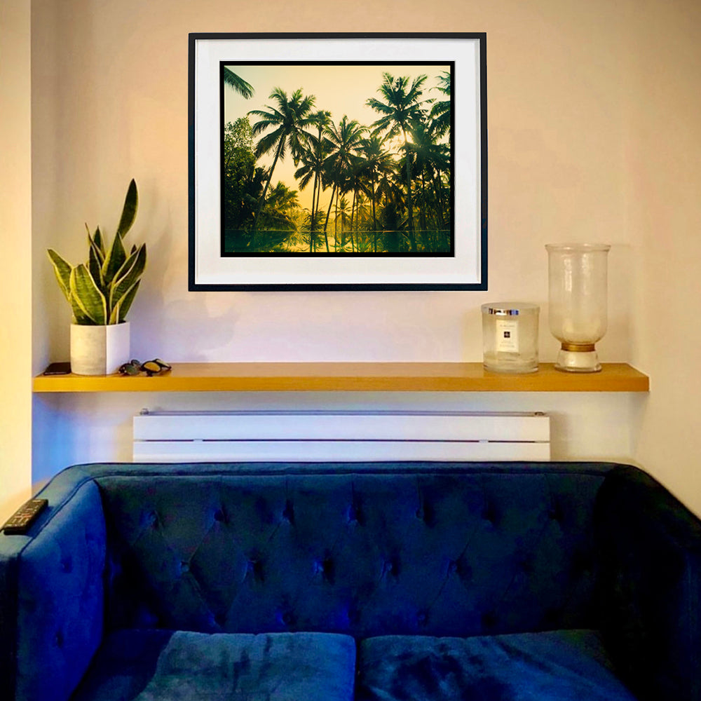 In situ black framed photograph by Richard Heeps. Green palms trees against a warm golden sky, and reflected in a pool below.