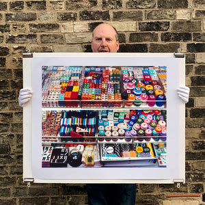 Photograph held by photographer Richard Heeps. Three compartmentalised shop shelves, each compartment has coloured plastic dice, counters, circular containers, cards, poker chips, and other plastic type games items.