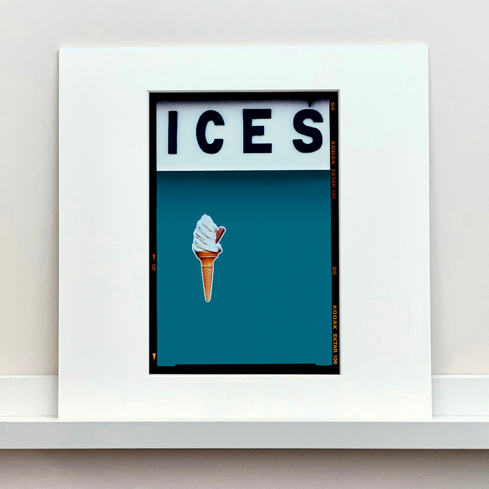 Mounted photograph by Richard Heeps.  At the top black letters spell out ICES and below is depicted a 99 icecream cone sitting left of centre against a blue teal coloured background.  