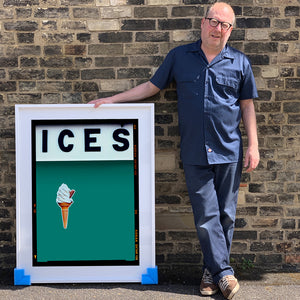 White framed photograph held by photographer Richard Heeps.  At the top black letters spell out ICES and below is depicted a 99 icecream cone sitting left of centre against a deep green teal coloured background.  