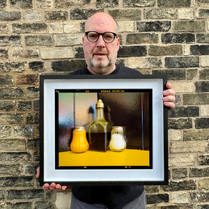 Richard Heeps holding Pepper, Vinegar and Salt cafe condiments still life photograph in a small black frame.