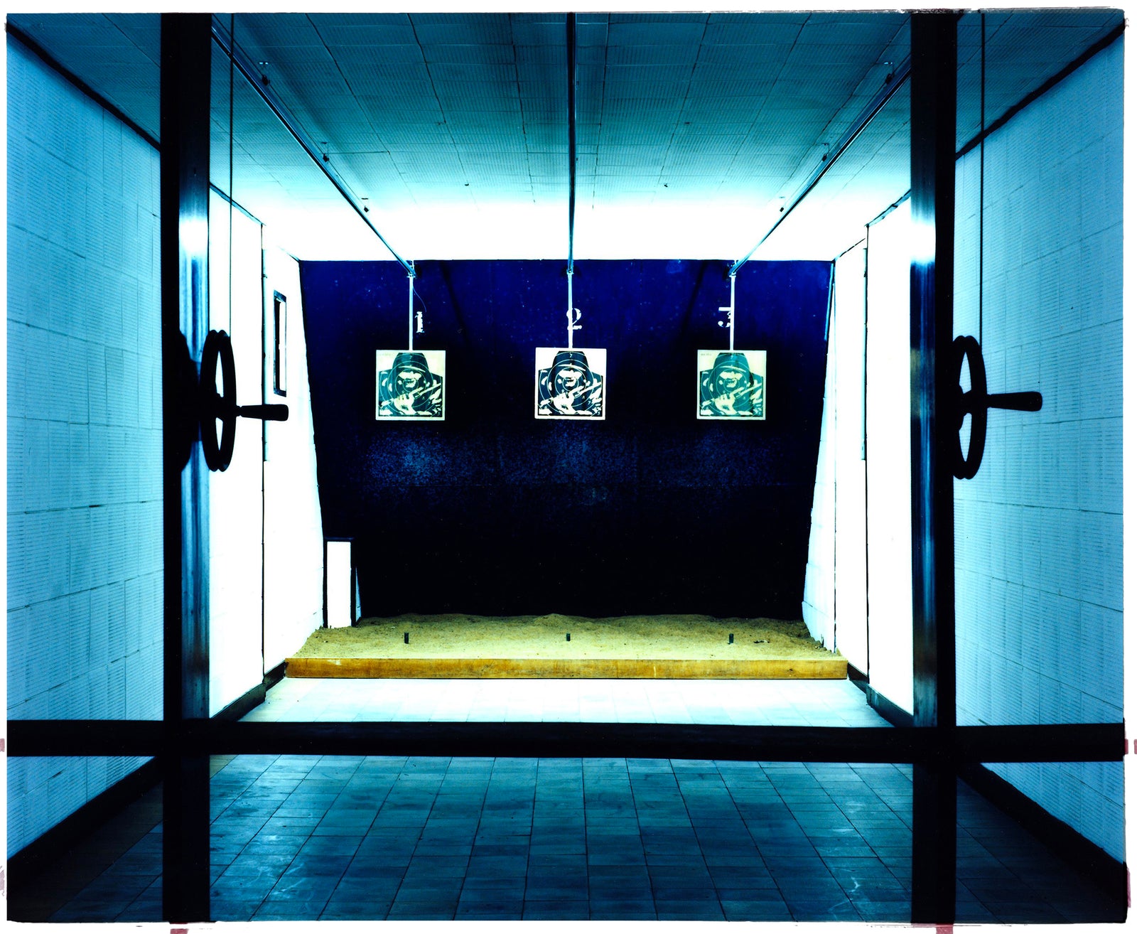 Photograph by Richard Heeps. A shooting range with 3 targets depicting soldiers. The back drop is blue surrounded by neon giving the whole range a blue glow.