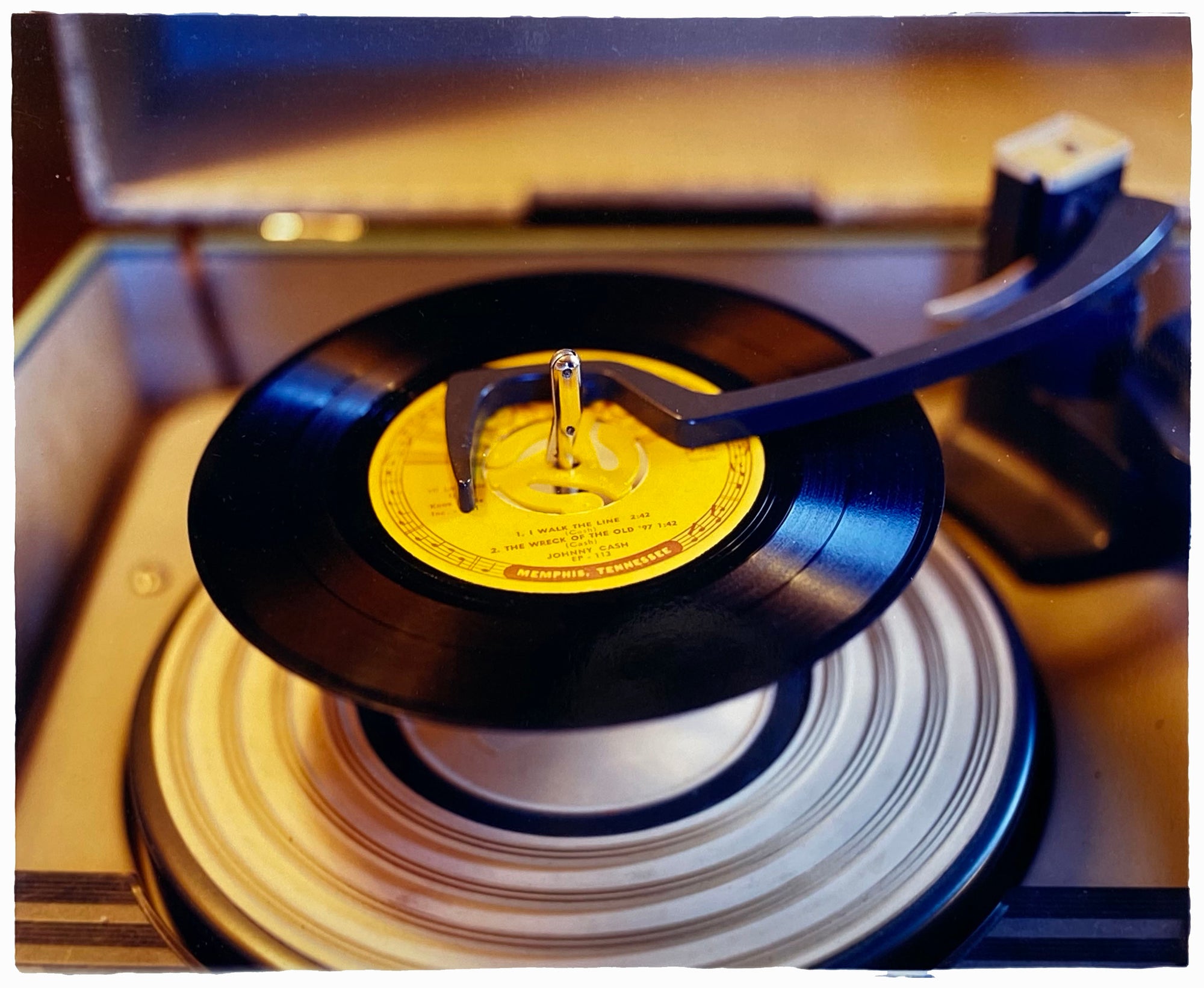 Photograph by Richard Heeps. A black vinyl with a yellow label sits high on the spindle of a deck under the overarm.