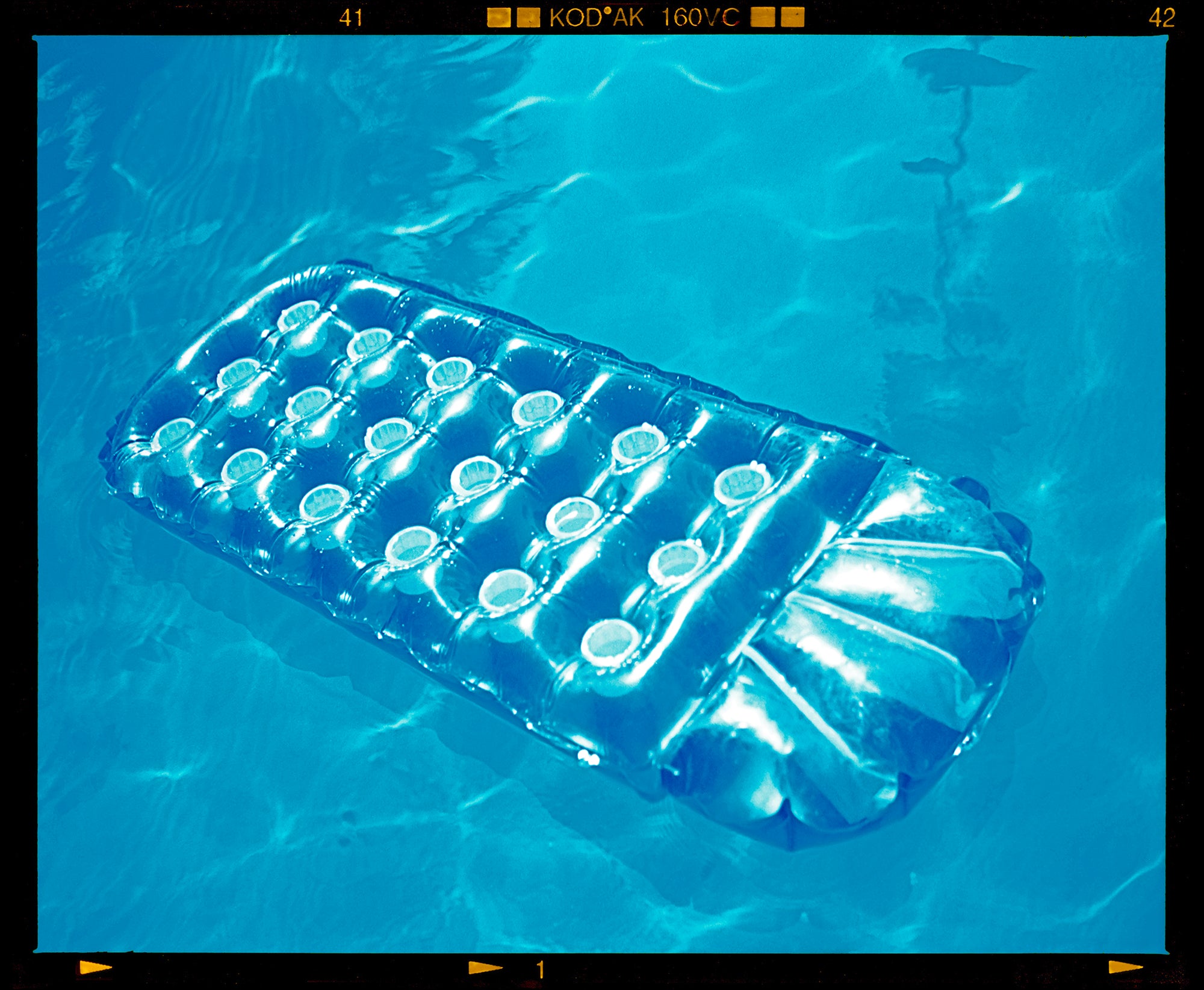 Photograph by Richard Heeps. A transparent blue lilo is sun bathing on a blue pool. 