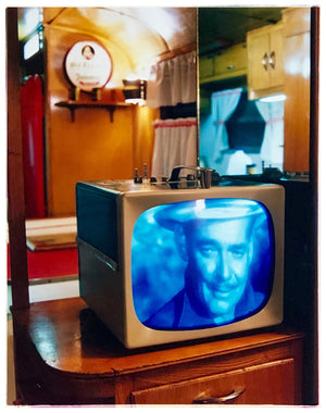 Photograph by Richard Heeps. A retro small brown television sits on a wooden table displaying a black and white film, with the face of Clark Gable filling the screen, it shows as blue and white. In the background of the television is a warm wood-panelled light.