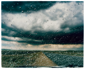 Windscreen, rain through a car window with dark clouds on a road in South Africa, landscape photograph by Richard Heeps.