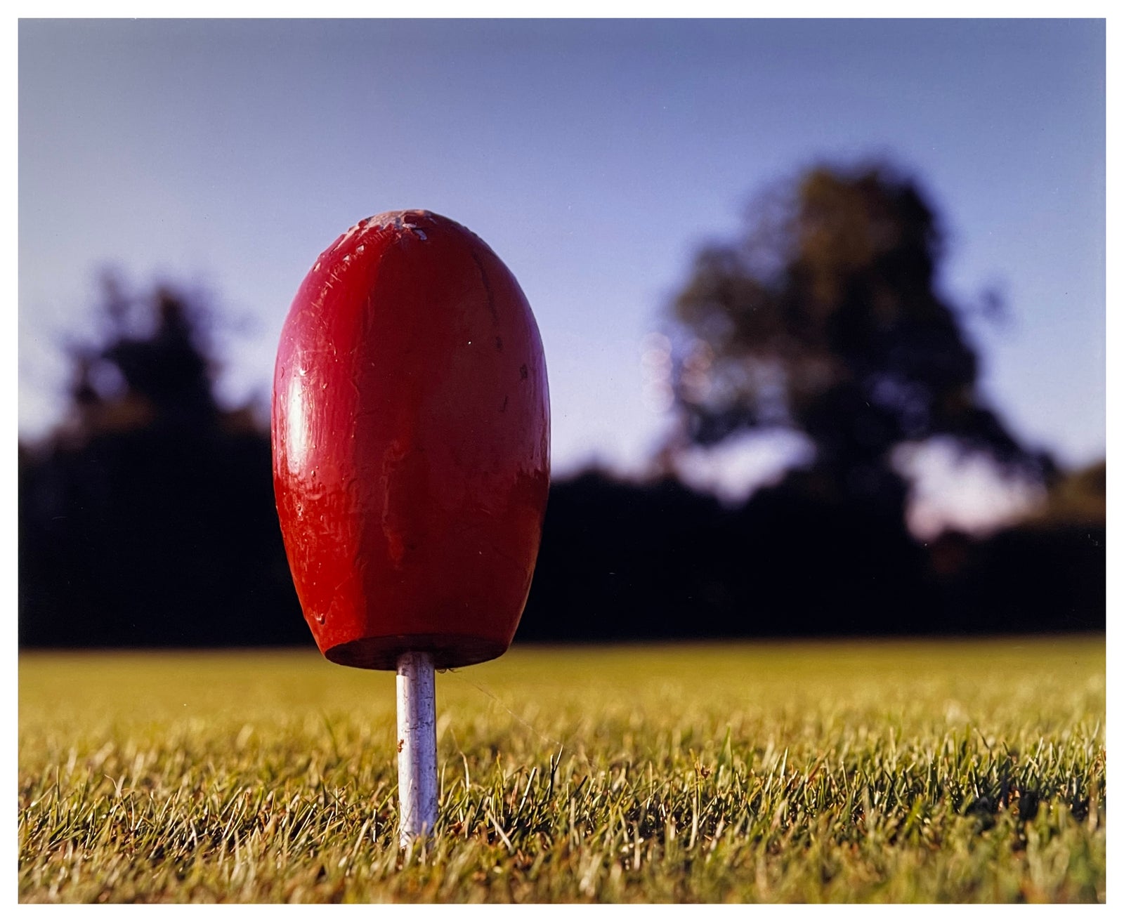 Photograph by Richard Heeps.  A slightly battered Lady Tee Marker fills the picture standing on the grass with blurred trees and sky in the background.