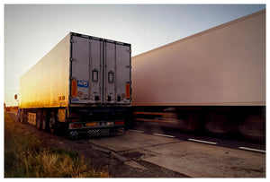 Photograph by Richard Heeps.  A lorry sits in a layby whilst another one overtakes.  The lorries are lit by sunset.