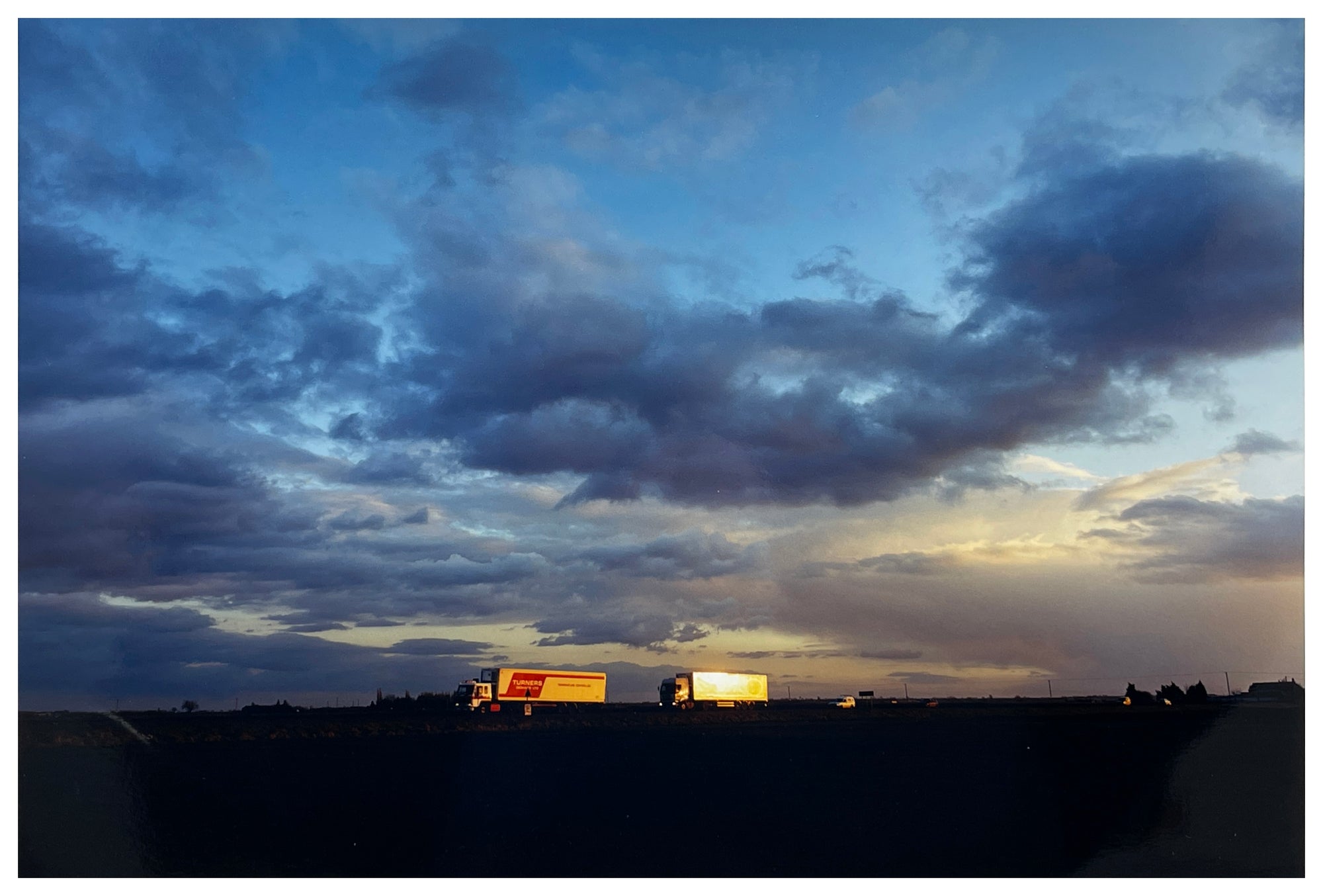 Photograph by Richard Heeps.  Lorries travelling along the A141 in a blue and cloudy dusk sky.