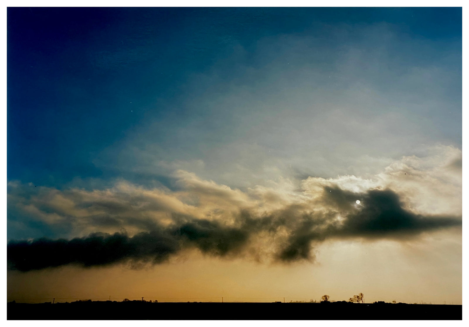 Photograph by Richard Heeps.  Evening clouds sit in the night sky above a dark, fen landscape.