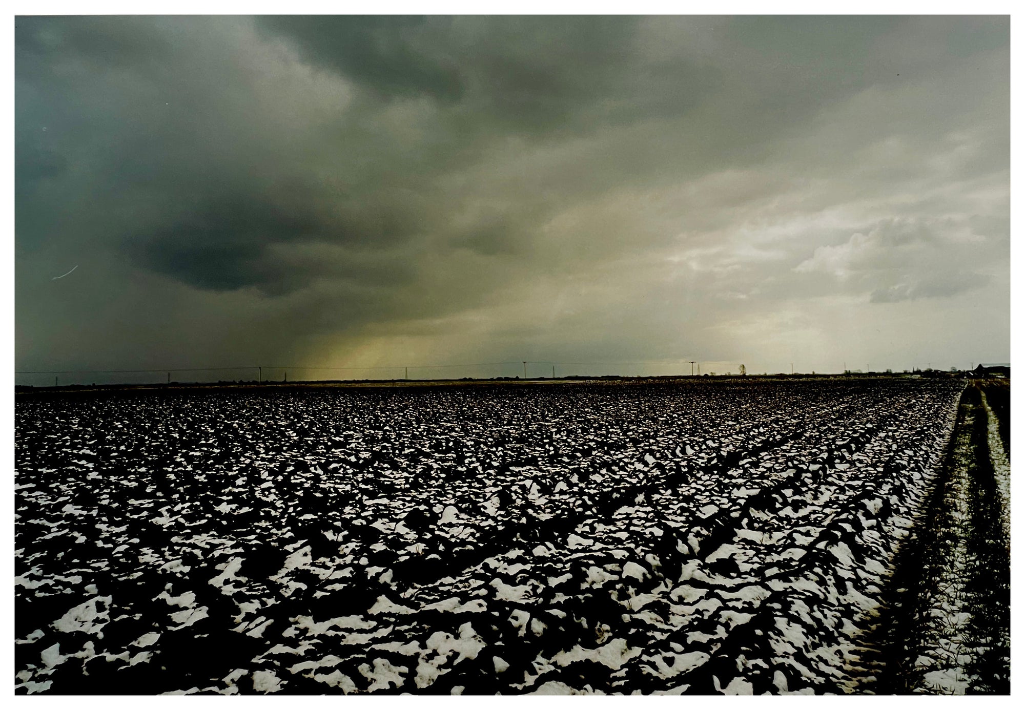 Photograph by Richard Heeps.  A snow covered, deeply trenched, peat fields sits below a thick cloud which is bringing in a storm.
