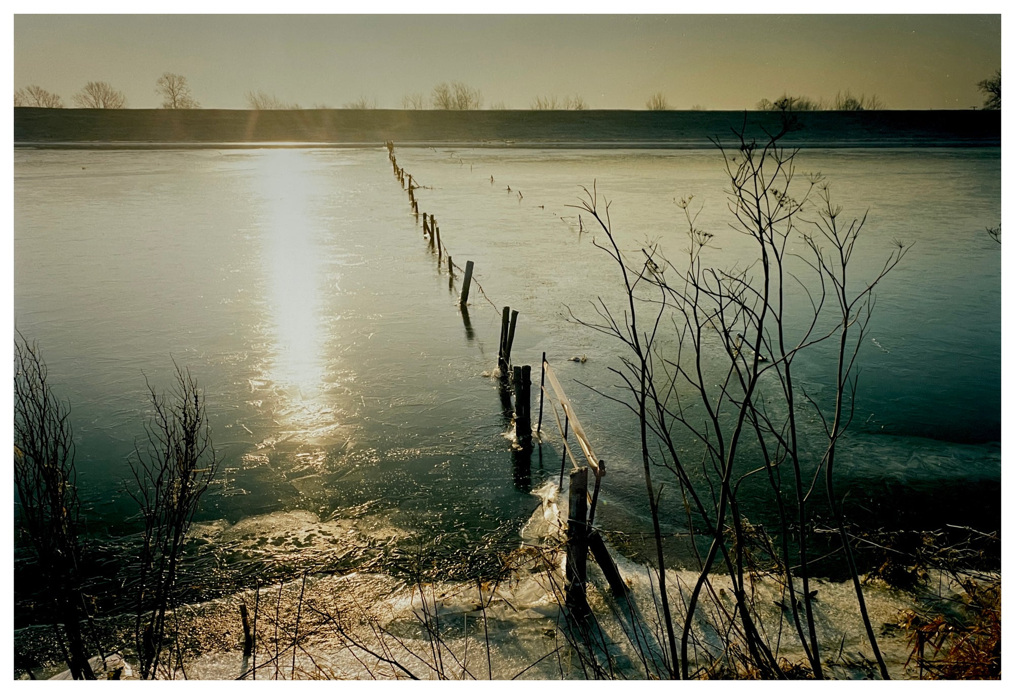 Photograph by Richard Heeps.  The wash sits frozen with a fence running through the middle of it.  Running parallel to the fence is shaft of sunlight from the setting sun.