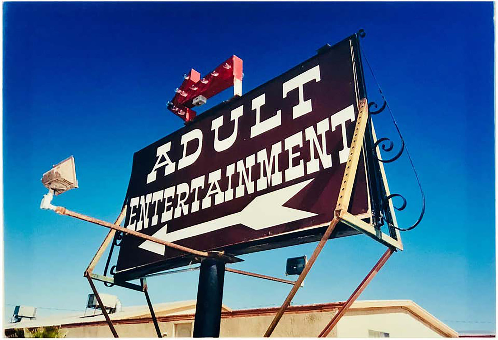 'Adult Entertainment' photographed in Beatty, Nevada, shows bold typography sitting prominently on an American road sign, against a background of bright blue sky. This fun and cheeky artwork was captured on a road trip through America and features in Richard Heeps' sold out book 'Man's Ruin'. An edition of this artwork recently sold at auction in The Auction Collective exhibition 'Hypercolor-Pop-Culture'.