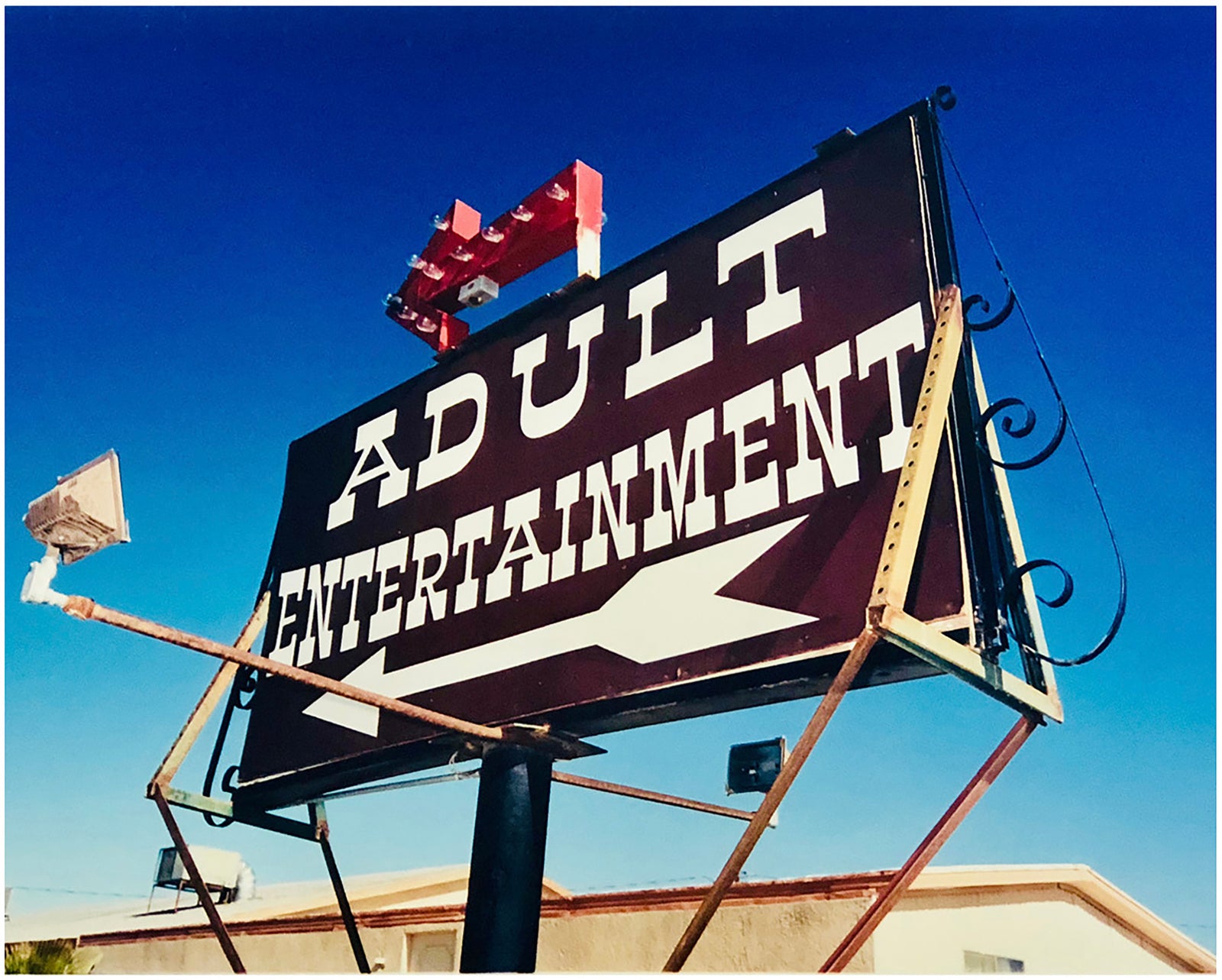 'Adult Entertainment' photographed in Beatty, Nevada, shows bold typography sitting prominently on an American road sign, against a background of bright blue sky. This fun and cheeky artwork was captured on a road trip through America and features in Richard Heeps' sold out book 'Man's Ruin'. An edition of this artwork recently sold at auction in The Auction Collective exhibition 'Hypercolor-Pop-Culture'.