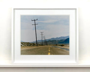 An open road in Amboy, California, featuring telephone poles disappearing into the mountainous distance. This classic and timeless landscape photograph is part of Richard Heeps' 'Dream in Colour' series. 