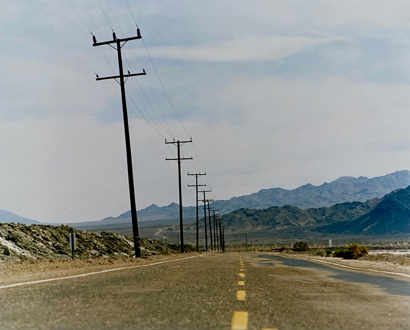 An open road in Amboy, California, featuring telephone poles disappearing into the mountainous distance. This classic and timeless landscape photograph is part of Richard Heeps' 'Dream in Colour' series. 