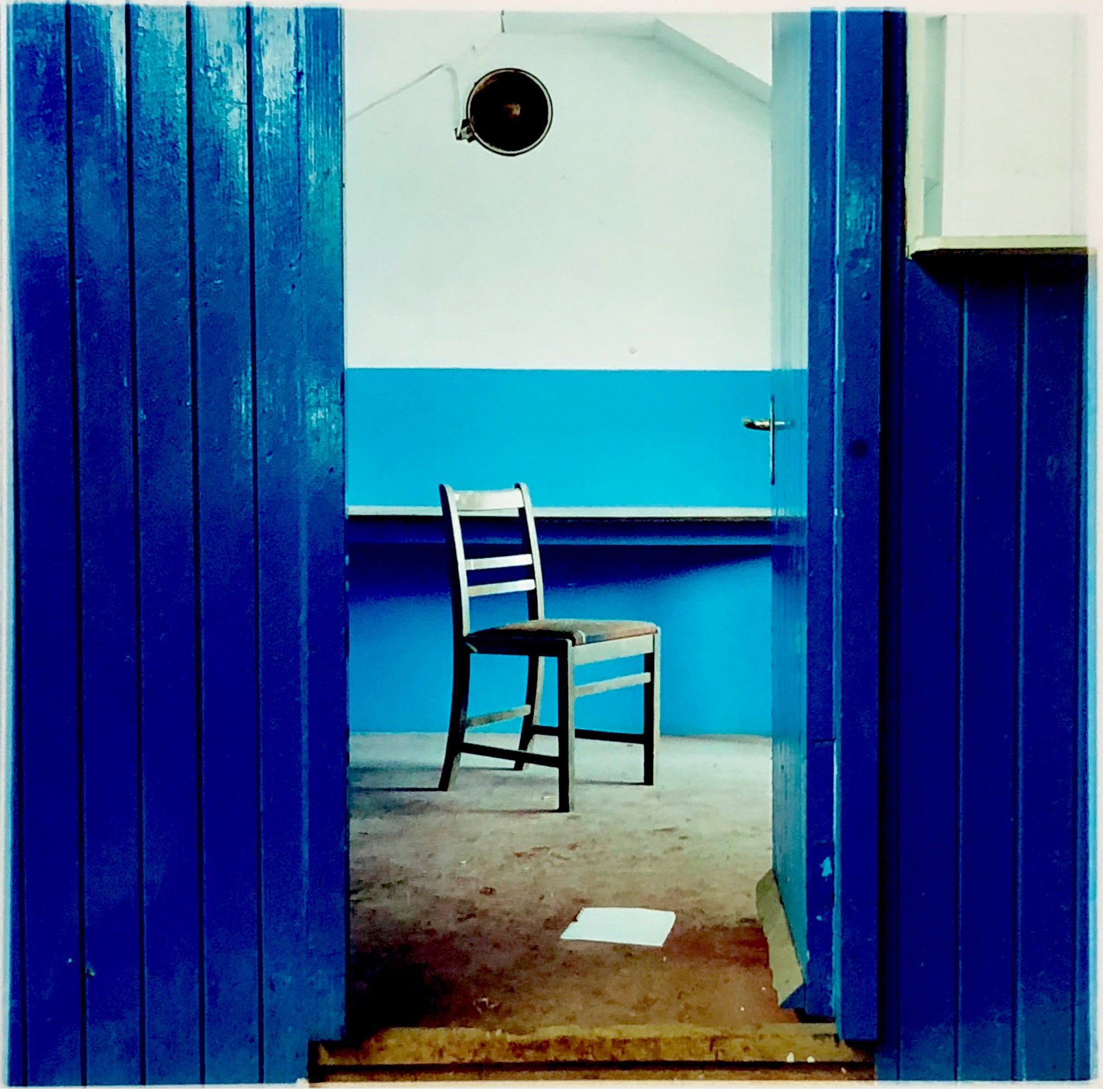 A blue painted room with a solitary chair visible through an open door