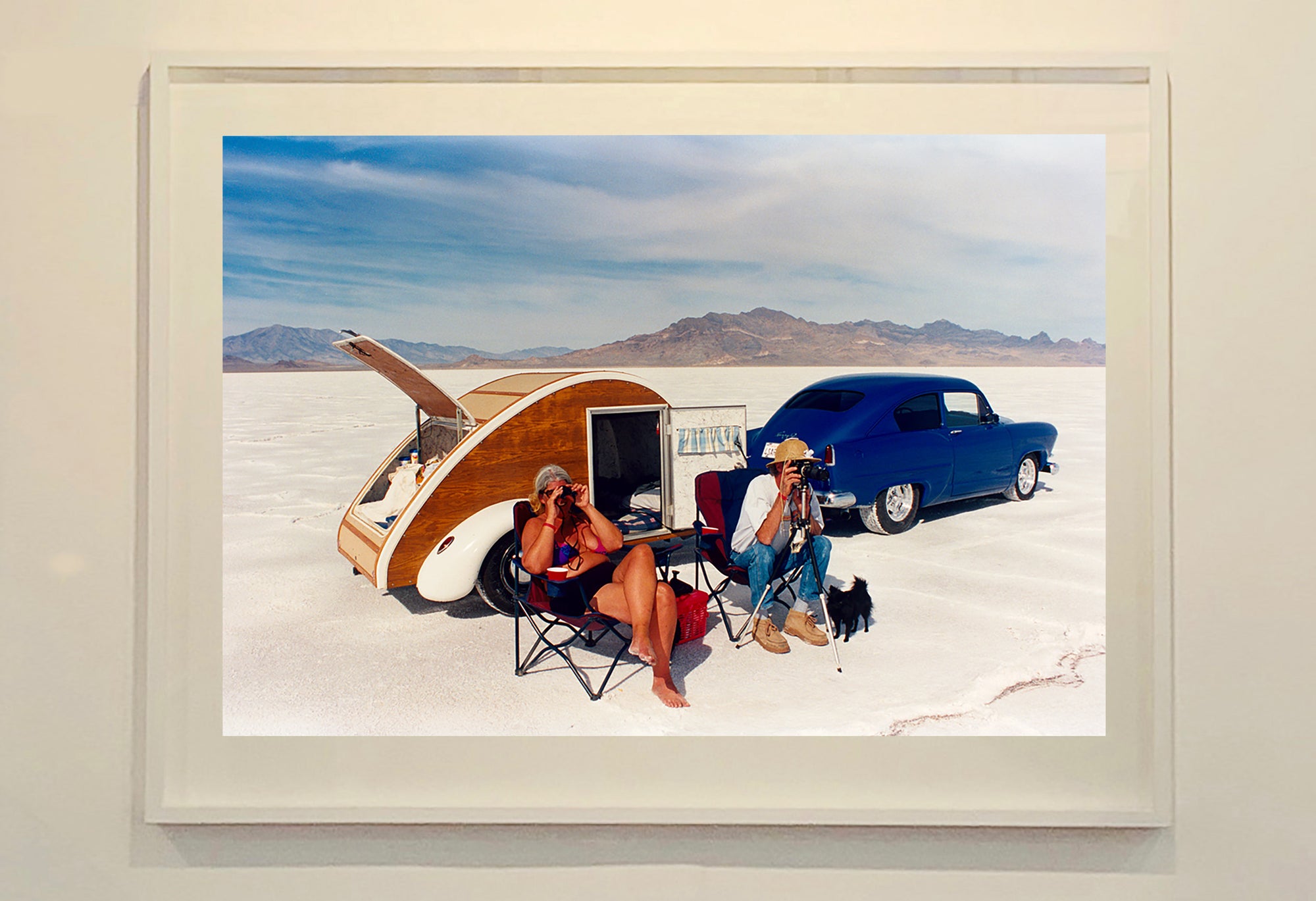 'Christine's '52 Henry J & teardrop' was captured in Bonneville Salt Flats, Utah, the iconic home of speed. This photograph shows the mountains in the distance meeting and contrasting with the flatness of the salt pan, whilst a pair of retro spectators look out at the speeding cars in the distance.