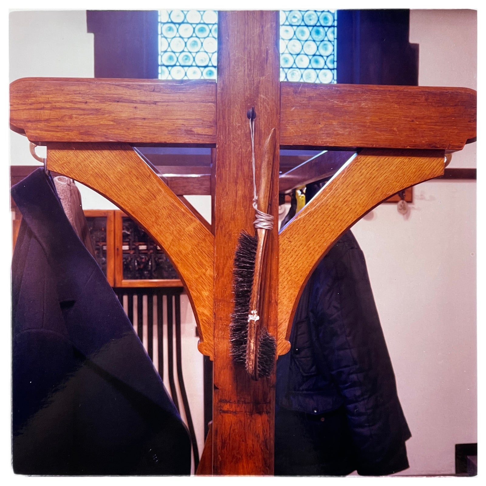 Photograph by Richard Heeps. A wooden coat stand with a coat brush hanging from a piece of string. 