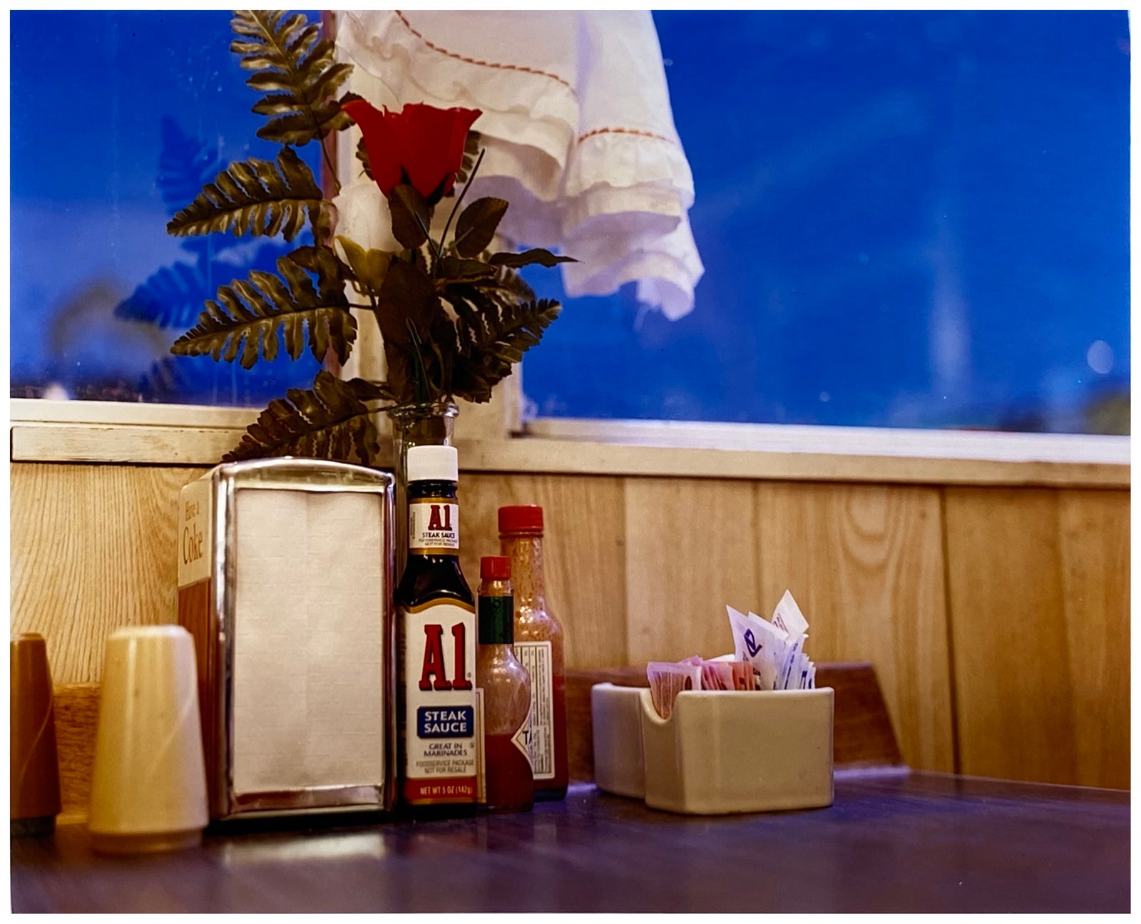 'Condiments' shows a classic American Diner table-scape, captured at the Bonanza Café in the small town of Lone Pine, California. This piece is part of Richard Heeps' 'Dream in Colour' series.
