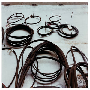 Photograph by Richard Heeps. A selection of different size drive belts hang on a set of nails. 