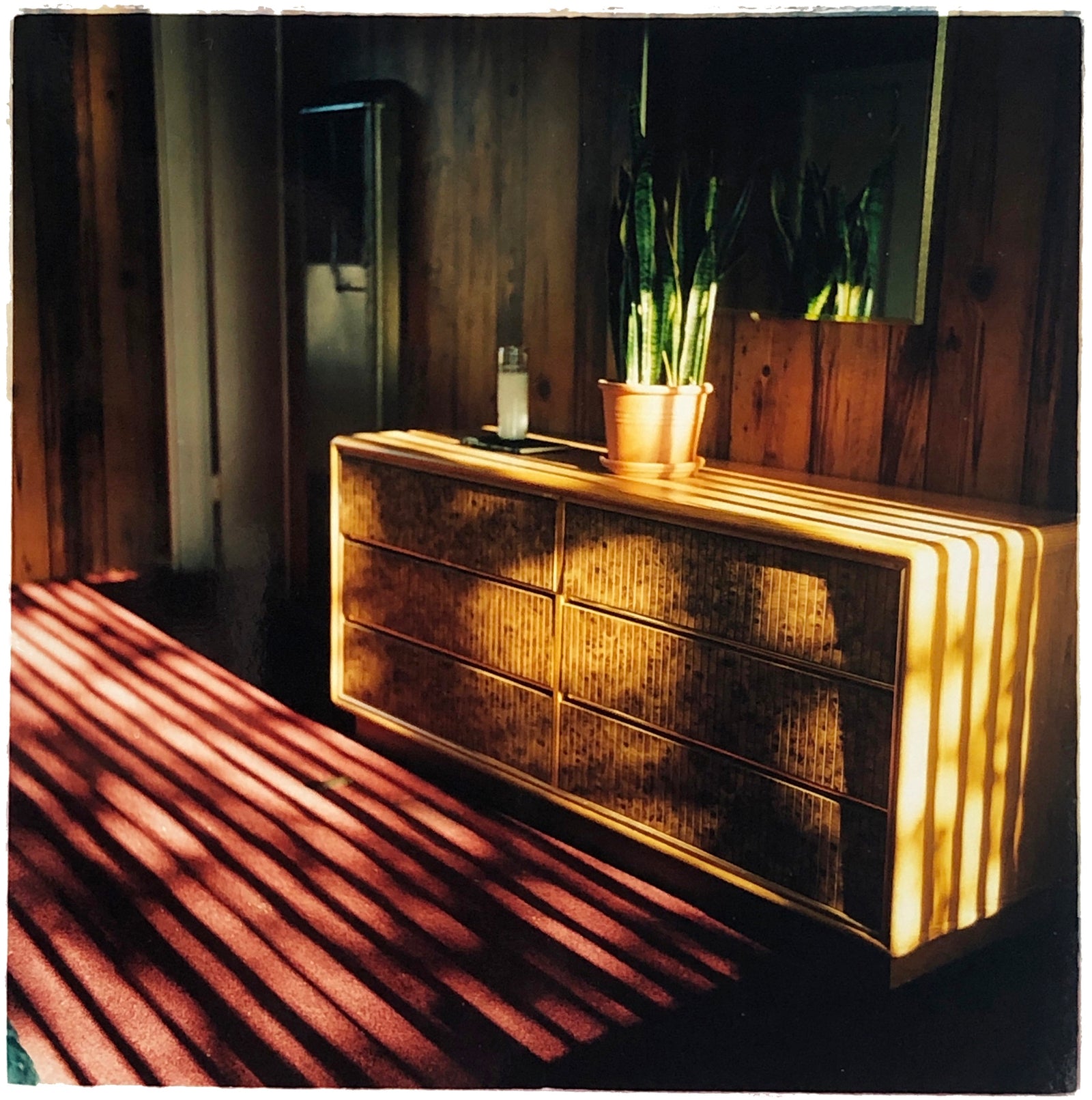 Light streams into the mid-century interior of the Harmony Motel, casting a patterned shadow across the rattan furniture and cactus. This cinematic motel room interior photograph taken in Twentynine Palms, California, is part of Richard Heeps' 'Dream in Colour' series.
