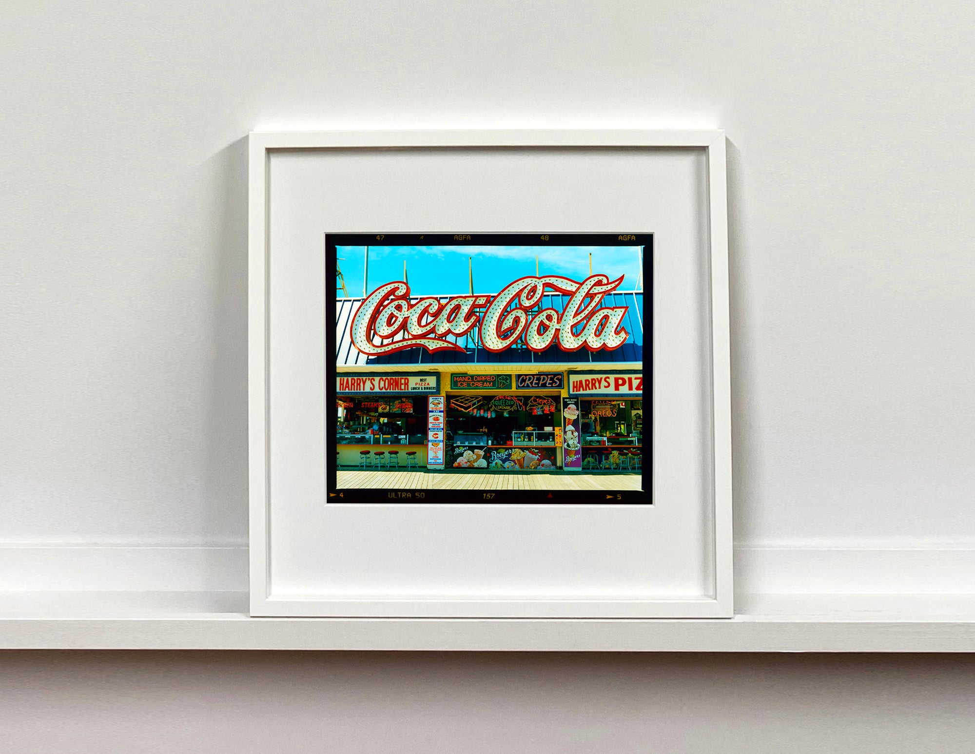 Harry's Corner, a photograph by Richard Heeps taken on the Wildwood boardwalk, featuring neon typography and the iconic Coca-Cola sign against a bright blue sky. 