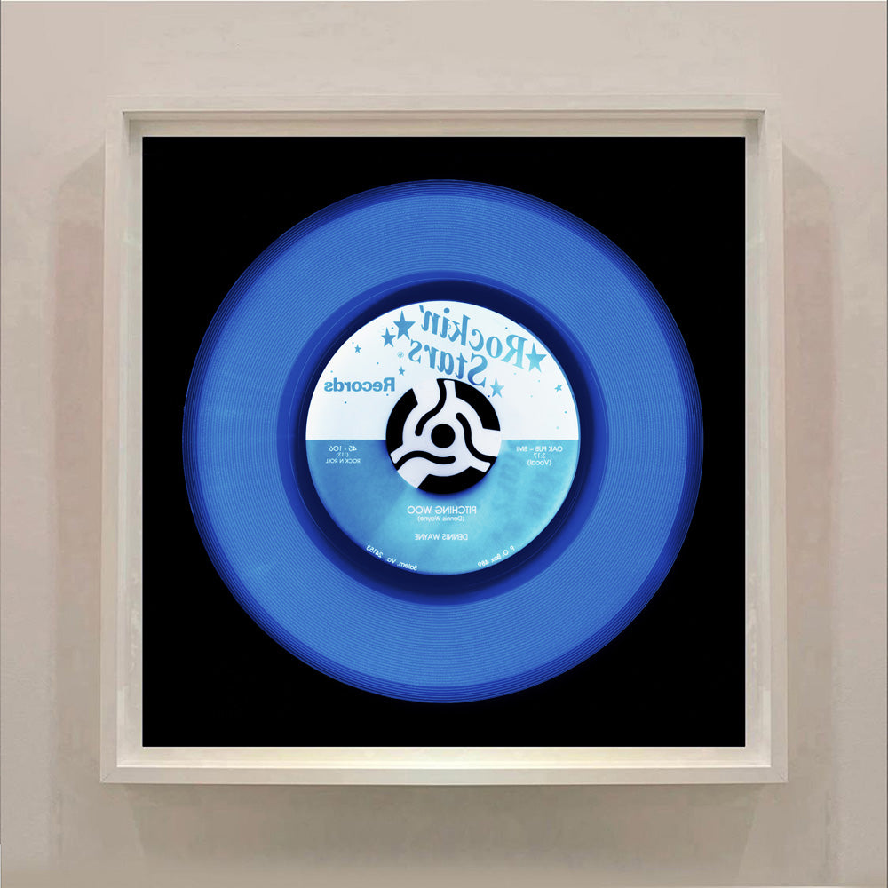 Photograph by Natasha Heidler and Richard Heeps.  A denim blue record with darker blue grooves and the record label is half white, half blue with writing in the opposite blue and white.  This vinyl sits on a black background.