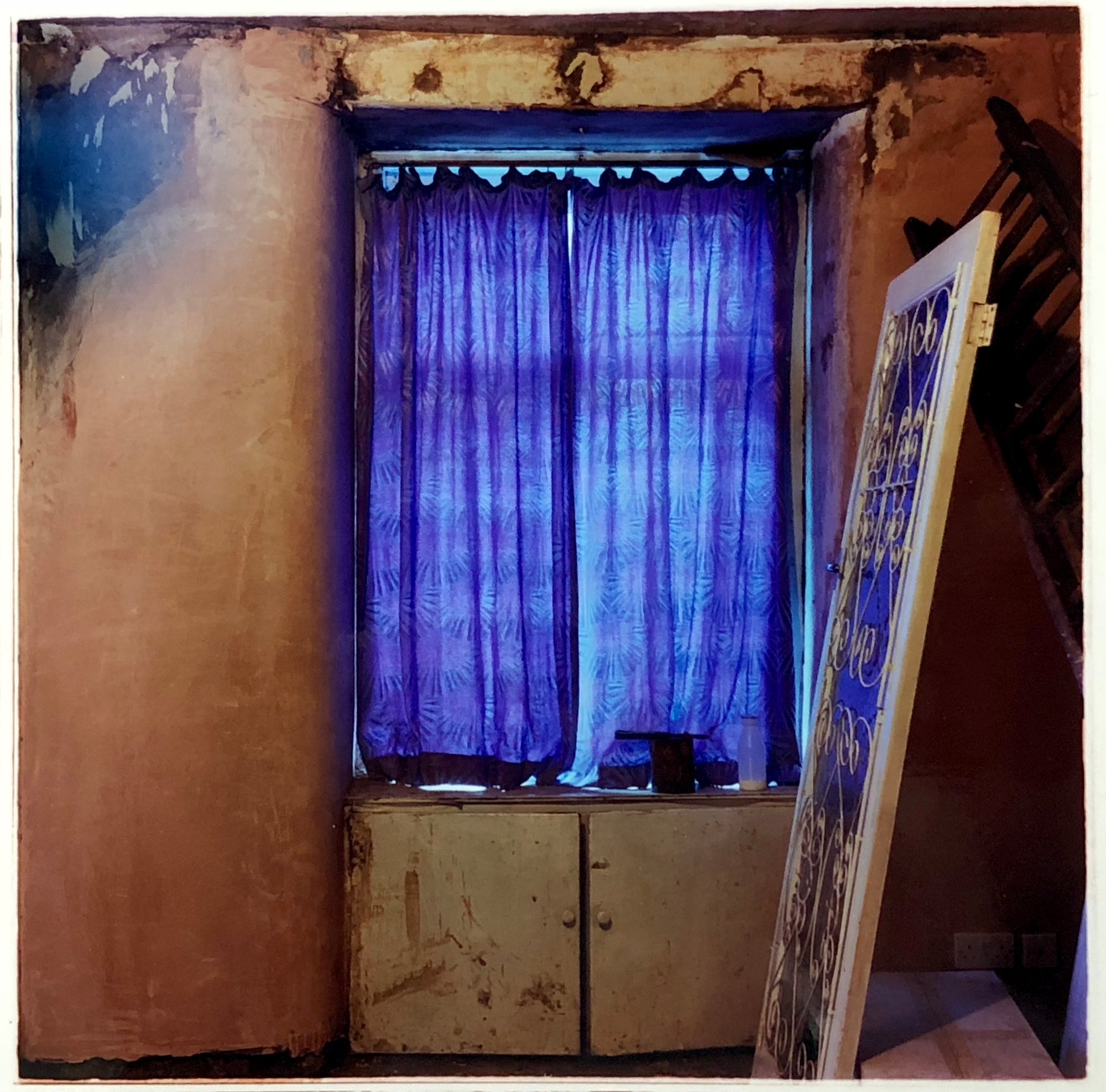Interior photography of a dilapidated home with a purple curtain.