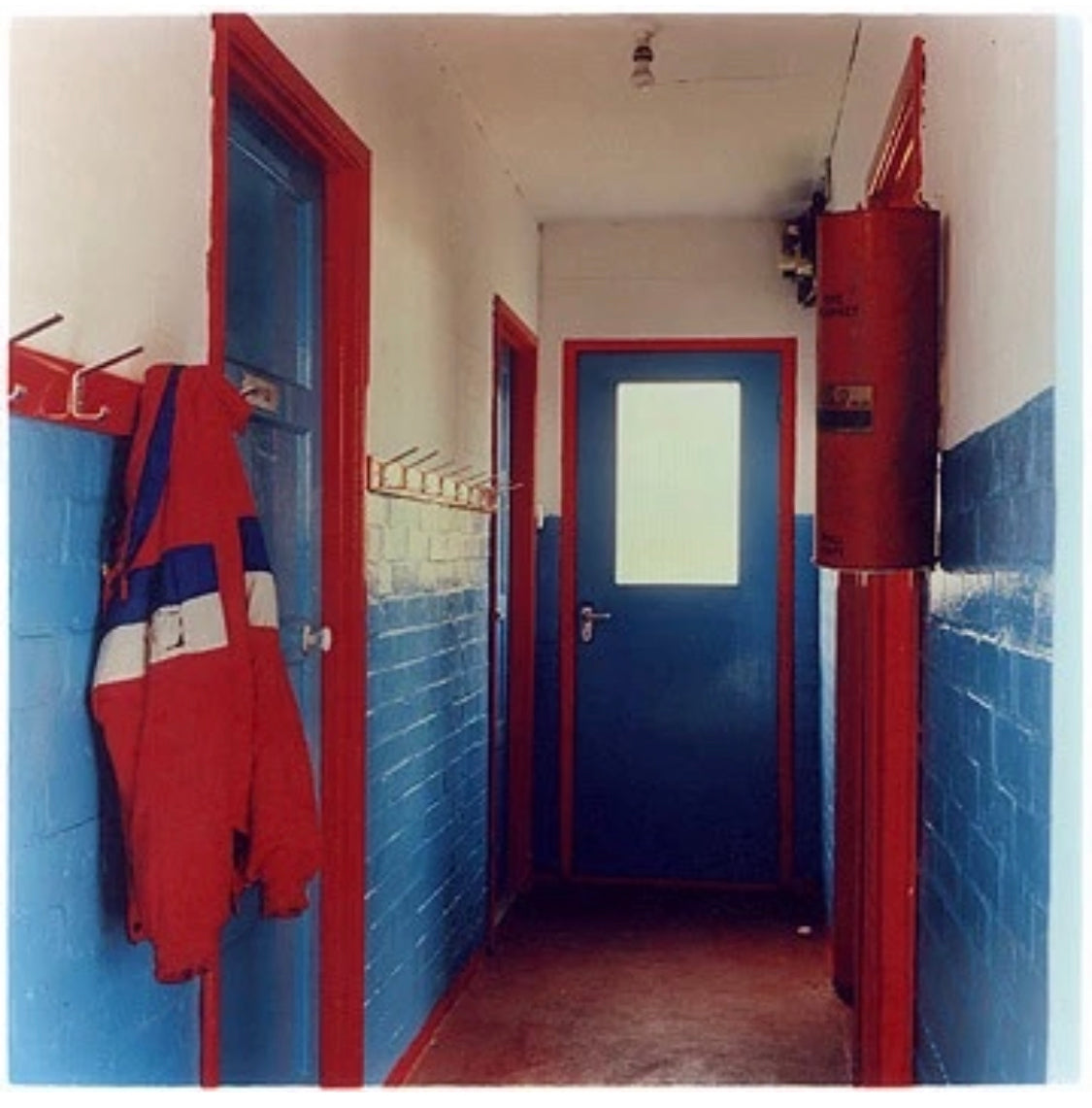 A jacket hangs from a row of coat pegs in a hallway painted blue, red and white.