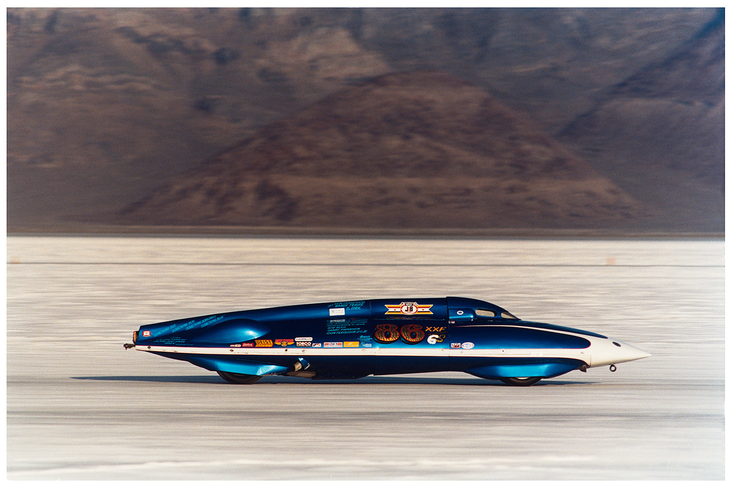 Blue racing car photograph by Richard Heeps against the landscape of Bonneville Salt Flats.